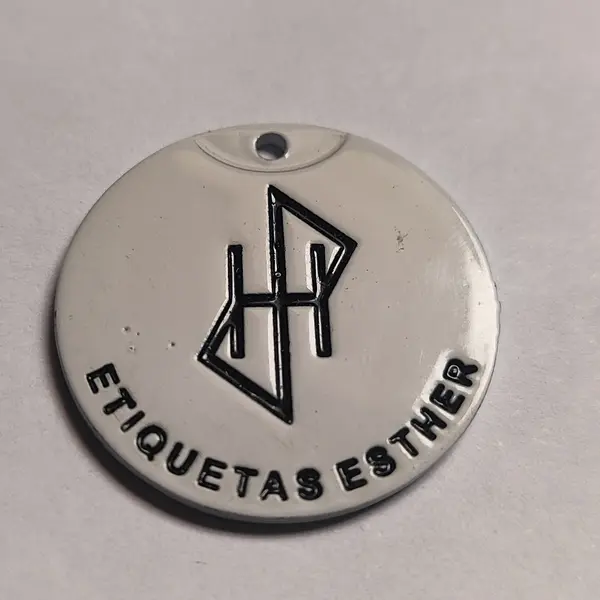 Medalla redonda de zamak en acabado blanco, en primer plano, con el monograma grabado en hueco