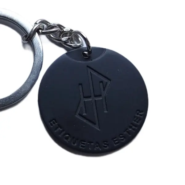 La misma medalla redonda de zamak en negro mate, en primer plano, con el monograma grabado en hueco