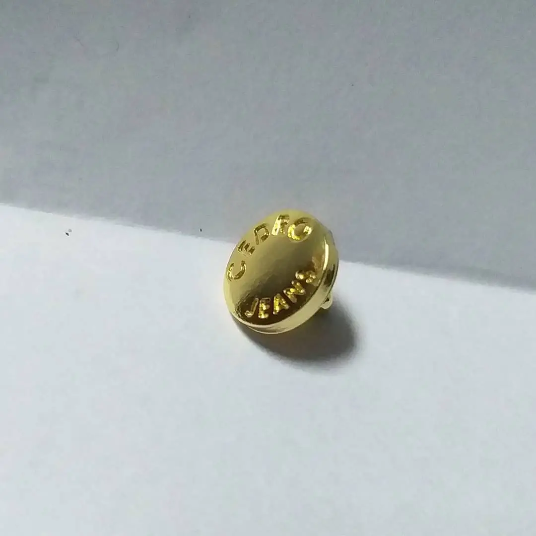 Botón metálico redondo en acabado dorado con el logo de una marca en relieve