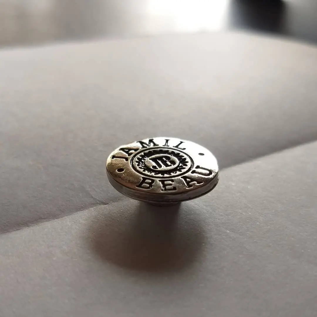 Botón metálico redondo en níquel brillante con el logo de una marca en relieve