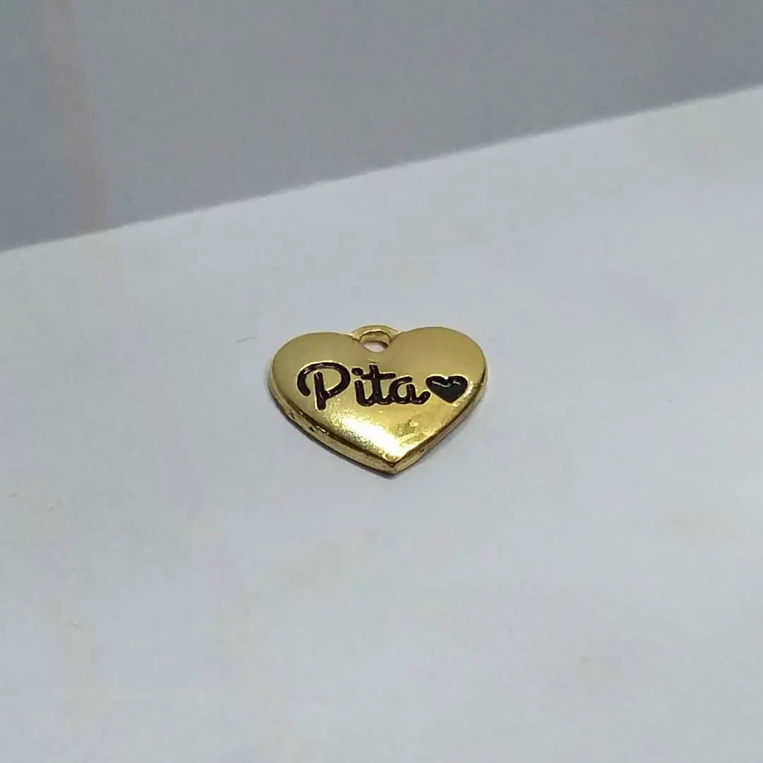 Dije de zamak en forma de corazón, acabado dorado, con el nombre de una marca grabado