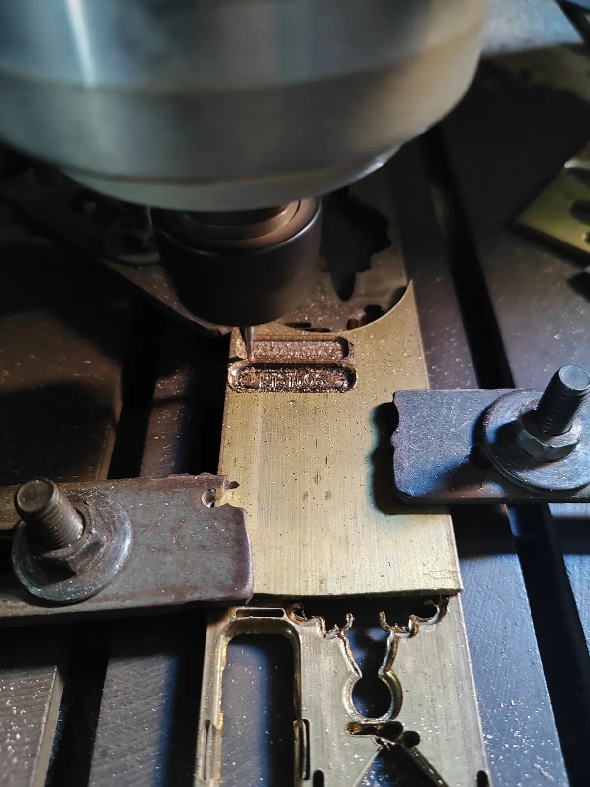 La fresa de la máquina CNC cortando el grabado de una marca en una matriz de latón, con la viruta acumulada alrededor